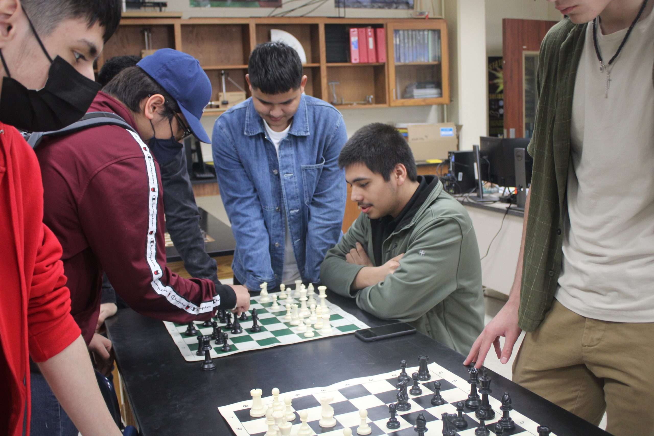 Multiple students gather around two chess matches.