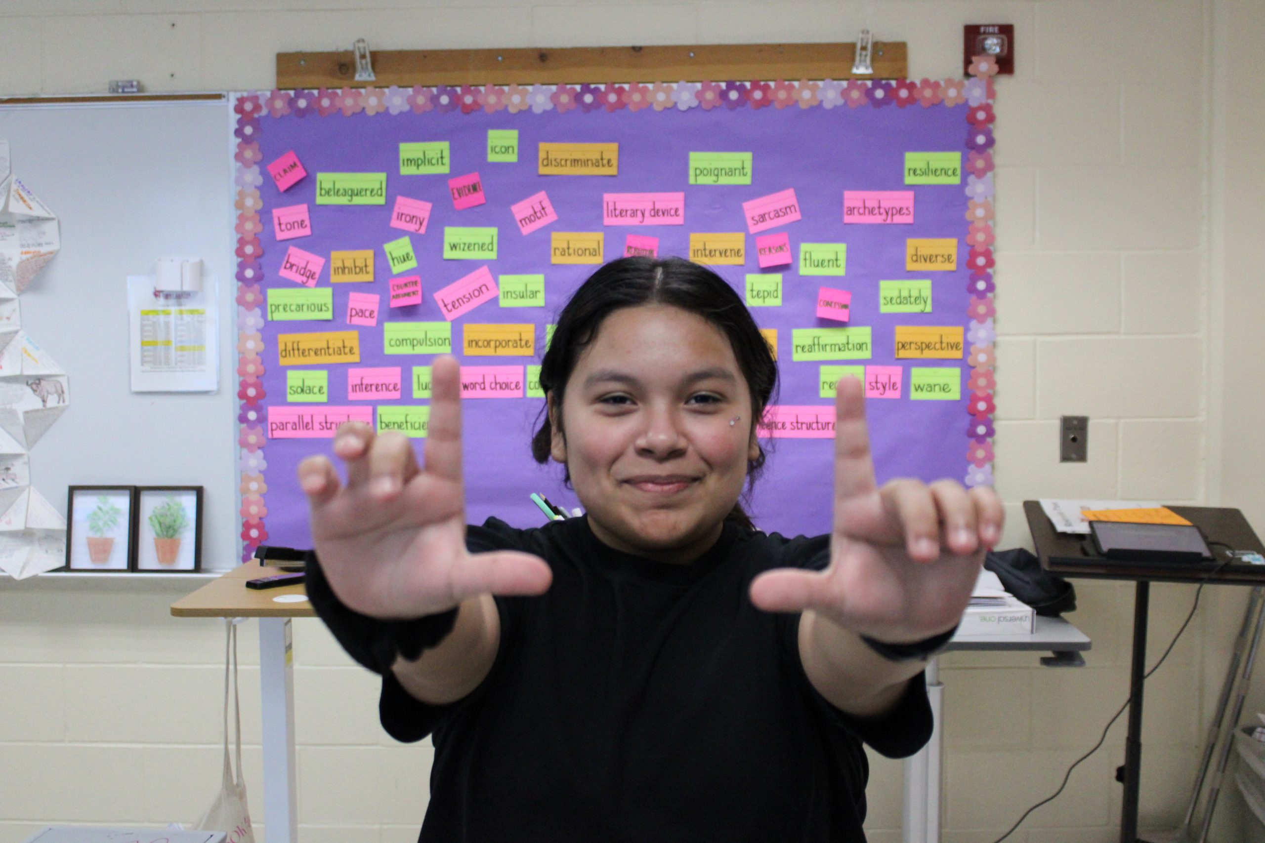Student raising her hands in front of a colorful vocabulary board.